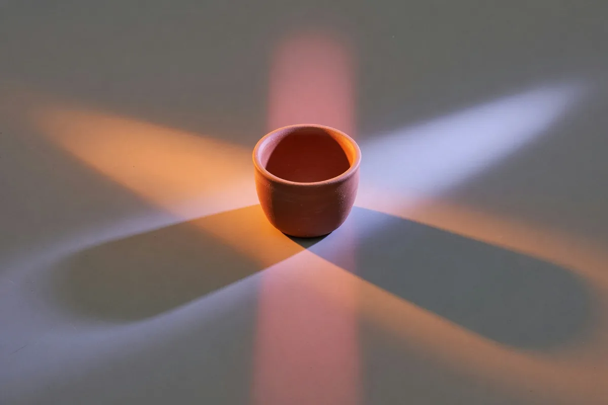 Un bol de terre cuite sur une table grise, éclairé par trois lumières qui jettent trois ombres