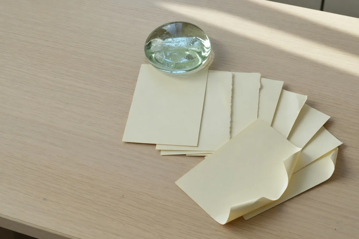 Sur un bureau clair, un presse-papier de verre retient quelques cartes crème, et d'autres ont glissé devant.