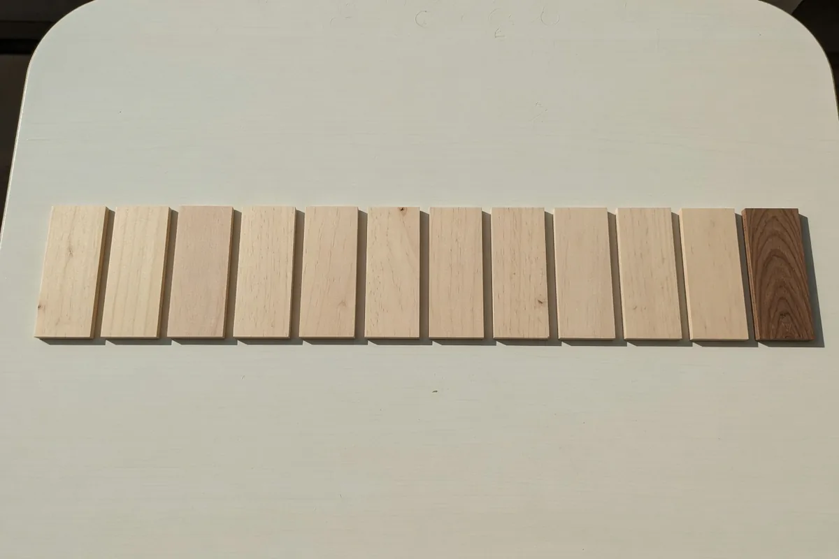 Une rangée de plaquettes de bois clair, la dernière taillée dans un bois sombre, dans le même alignement.