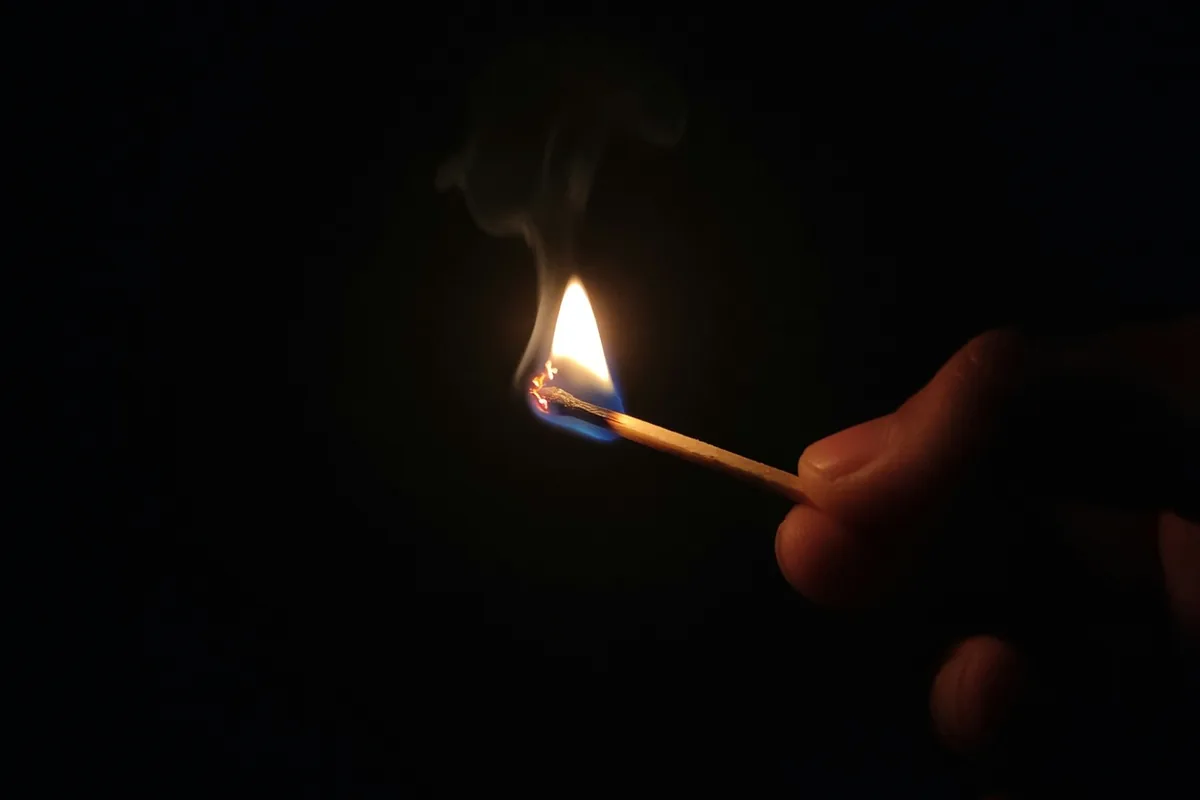 Dans le noir, une main tient une allumette dont la flamme est la seule lumière