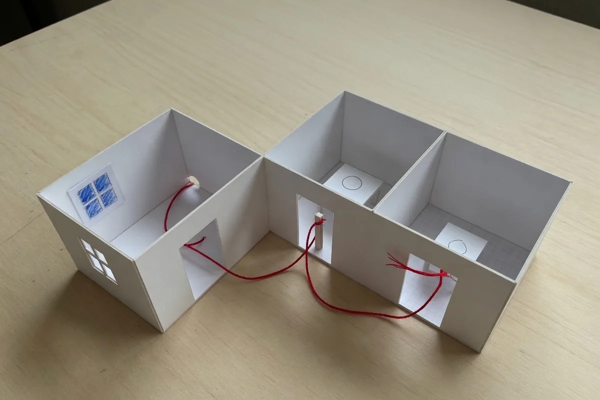 Maquette blanche de trois pièces reliées, un fil rouge passe par toutes les portes, sur une table nue